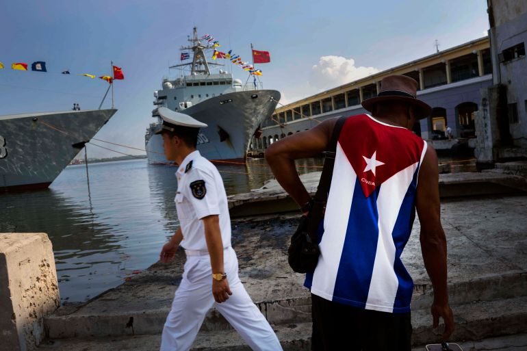 Ein Mann, der ein Hemd mit kubanischer Flagge trägt, betrachtet ein chinesisches Marineschiff im Hafen von Havanna, 2015 | Bildquelle: Al Jazeera © Ramon Espinosa/The Associated Press | Bilder sind in der Regel urheberrechtlich geschützt